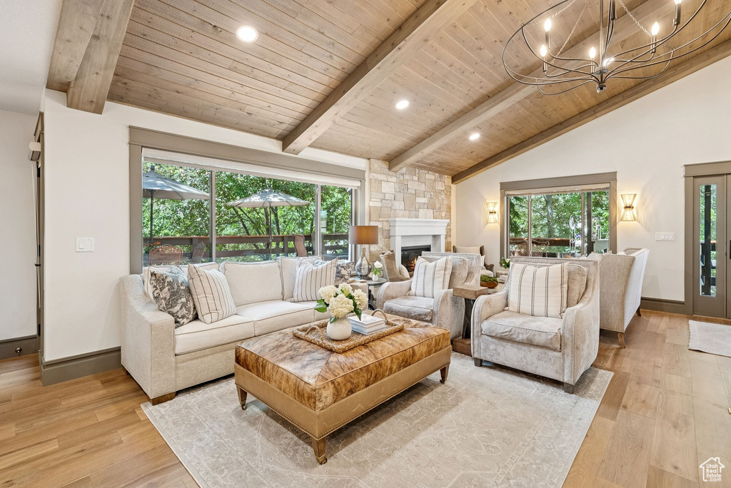 Living room featuring healthy amount of natural light, light wood finished floors, wooden ceiling, a large fireplace, and a chandelier