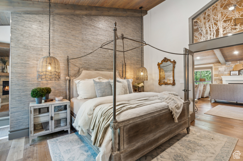 Bedroom with a lit fireplace, wood ceiling with exposed beams, a high ceiling, and wood finished floors