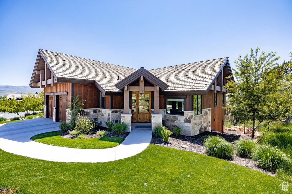 View of front of house with stone siding, a front lawn, a garage, and driveway