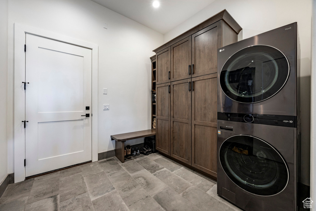 Washroom with stacked washer and clothes dryer, cabinet space, baseboards, and stone tile flooring
