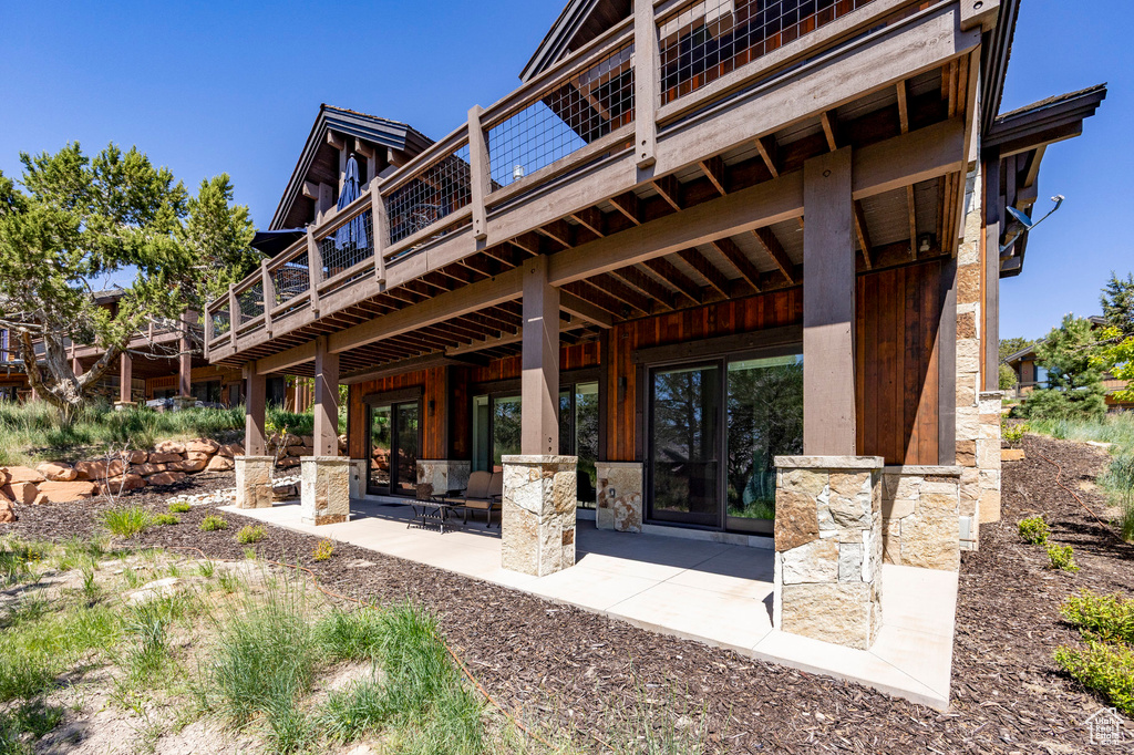 Rear view of house with a patio, stone siding, and a wooden deck