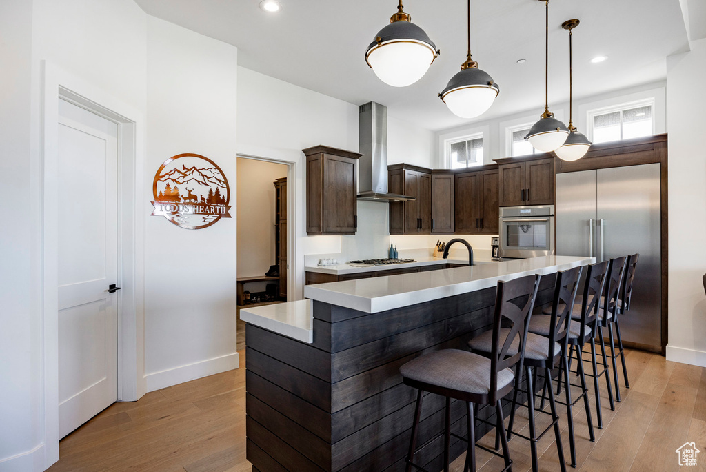 Kitchen featuring stainless steel appliances, wall chimney exhaust hood, dark brown cabinets, baseboards, and recessed lighting