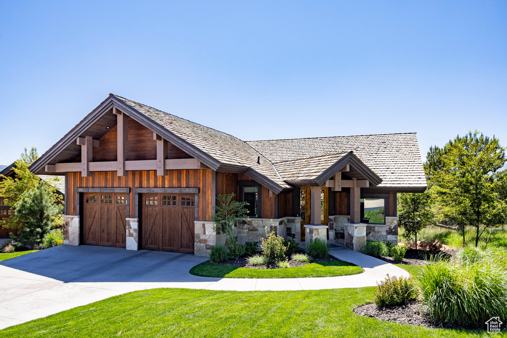 View of front of house with driveway, stone siding, a front lawn, and an attached garage