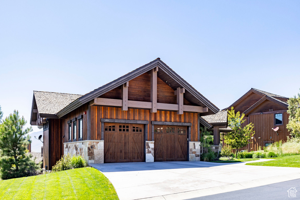 View of front of property featuring stone siding, concrete driveway, an attached garage, and a front lawn