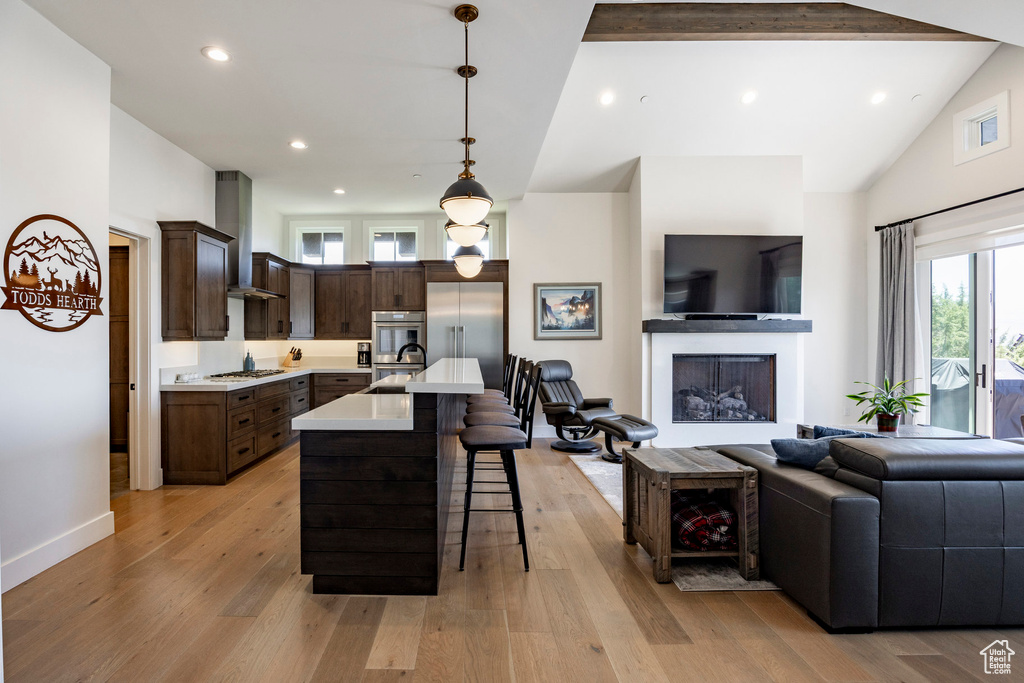 Kitchen featuring wall chimney exhaust hood, open floor plan, appliances with stainless steel finishes, a sink, and light countertops