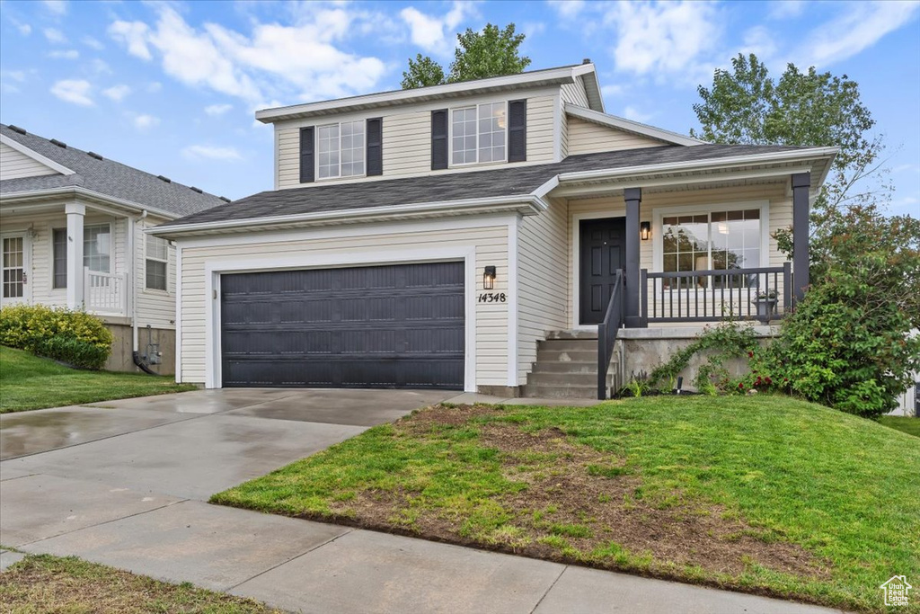 View of front of property with a front yard, covered porch, concrete driveway, and an attached garage