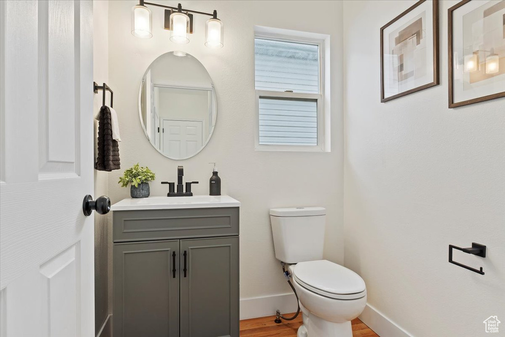 Half bath with vanity, toilet, wood finished floors, and baseboards