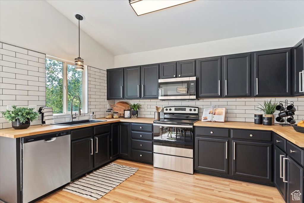 Kitchen with appliances with stainless steel finishes, a sink, wood counters, vaulted ceiling, and backsplash