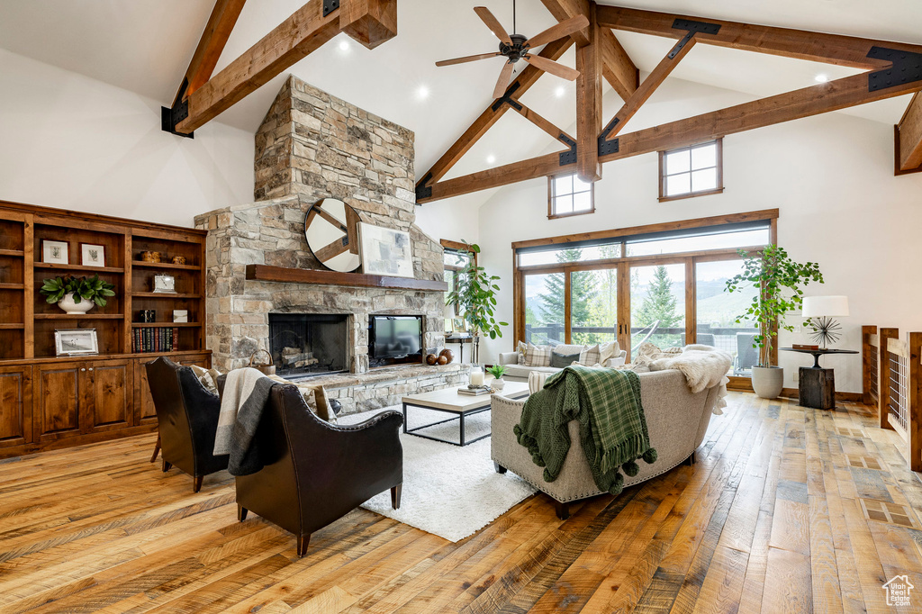 Living area featuring high vaulted ceiling, light wood-style flooring, beam ceiling, a ceiling fan, and a stone fireplace