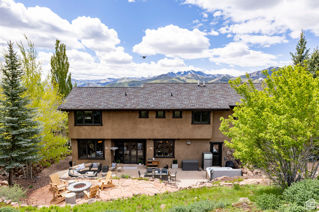Back of property featuring stucco siding, a patio area, a mountain view, and an outdoor living space with a fire pit