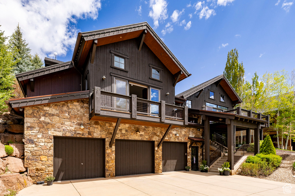Rear view of house featuring stone siding, an attached garage, a balcony, and driveway