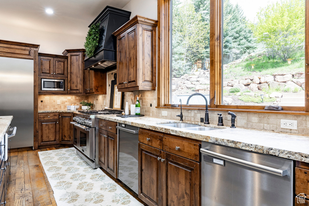 Kitchen featuring built in appliances, a sink, light stone countertops, tasteful backsplash, and premium range hood