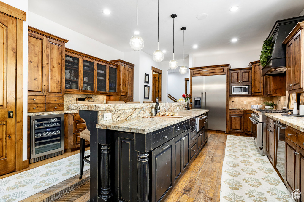 Kitchen with beverage cooler, built in appliances, a kitchen island, tasteful backsplash, and light wood-style floors