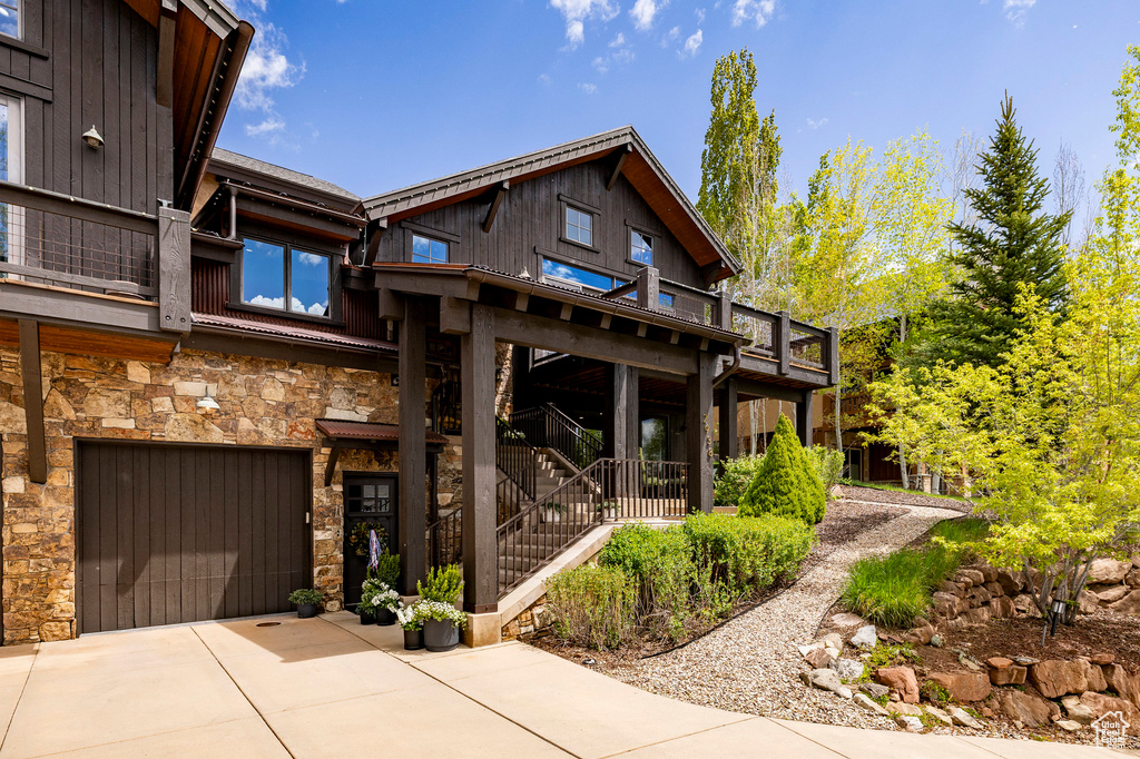 Back of property with concrete driveway, stone siding, an attached garage, and a balcony