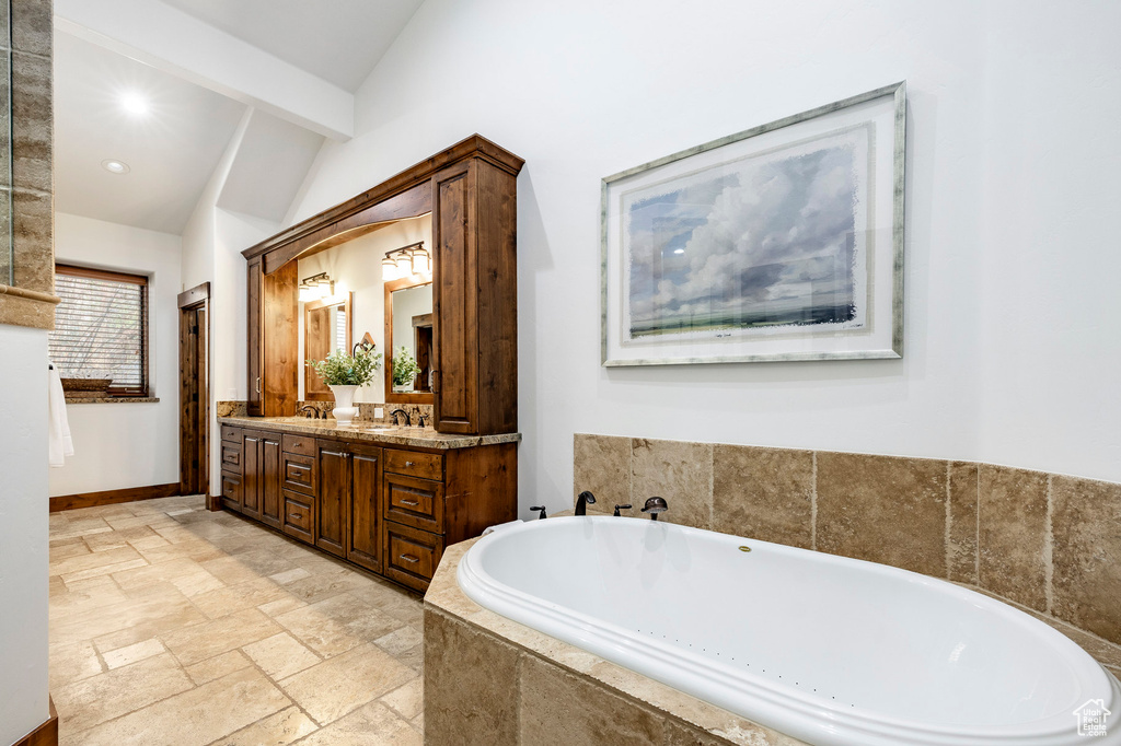 Bathroom with double vanity, a bath, stone tile flooring, recessed lighting, and baseboards