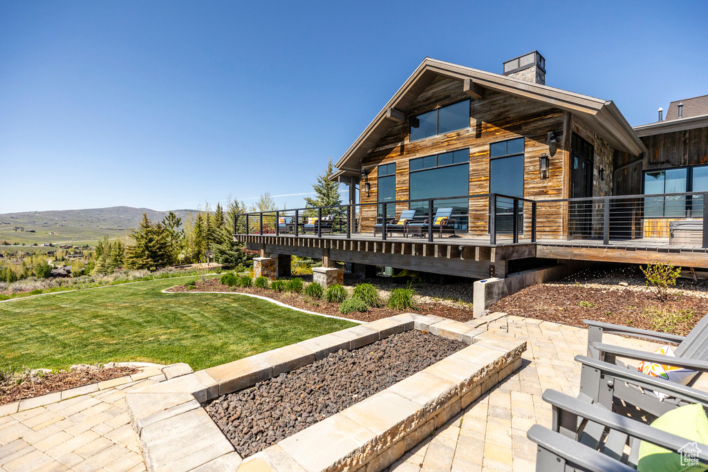Rear view of house with a chimney, a yard, a deck with mountain view, and a patio area