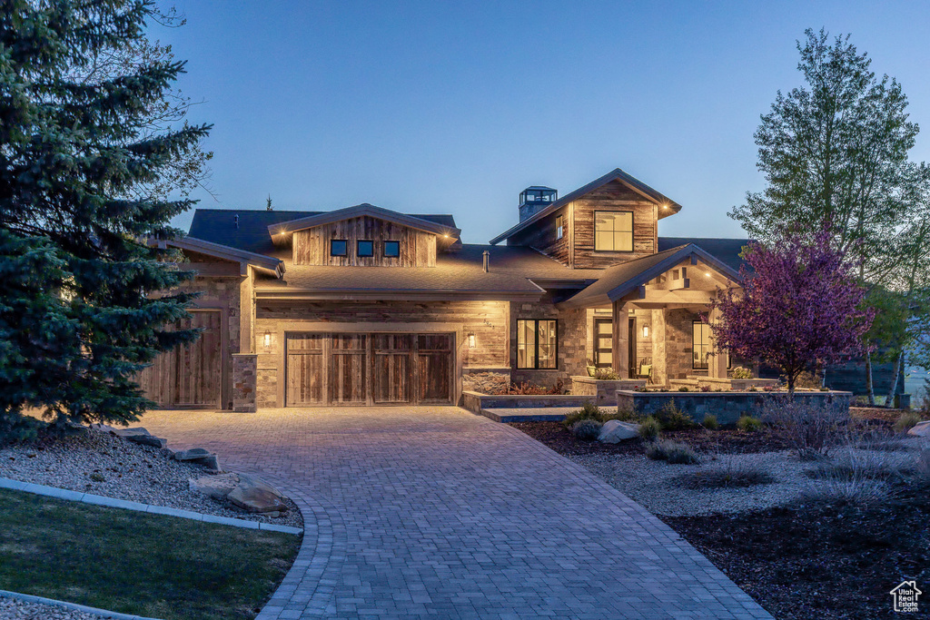 View of front of property featuring decorative driveway, a garage, stone siding, a chimney, and a porch