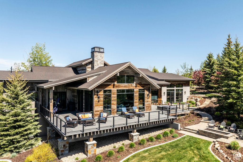 Back of property featuring a wooden deck, a chimney, and a yard