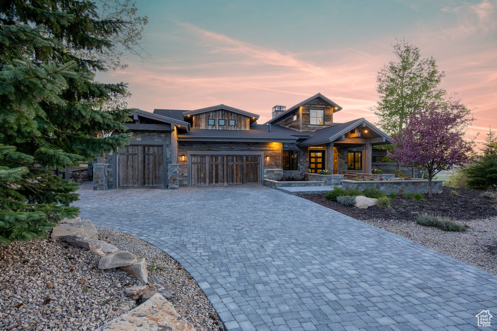 Contemporary house featuring stone siding, decorative driveway, a garage, and a porch