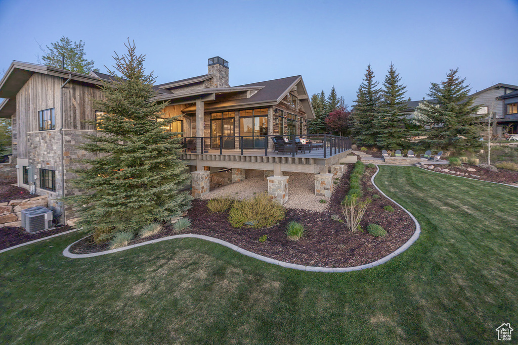 Rear view of property with a chimney, a deck, a lawn, central AC, and a sunroom