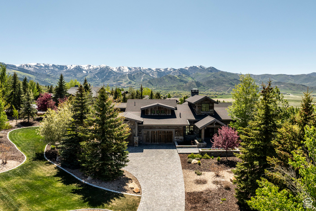 View of front facade featuring stone siding, a chimney, a mountain view, and driveway