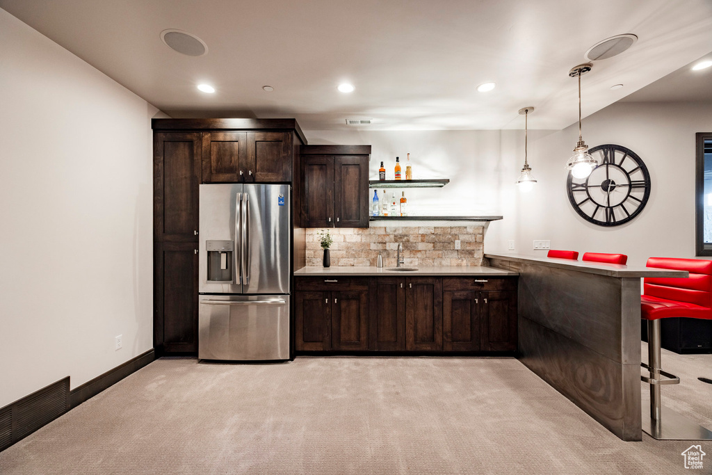 Kitchen with stainless steel refrigerator with ice dispenser, light carpet, a sink, dark brown cabinets, and light countertops