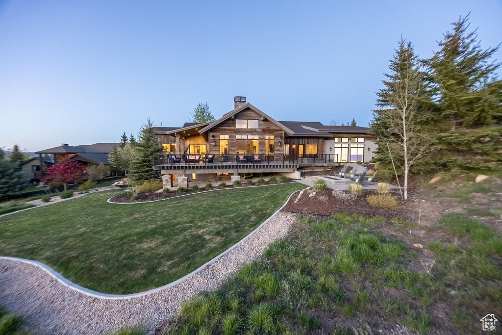 Back of house featuring a chimney, a yard, a deck, and stone siding