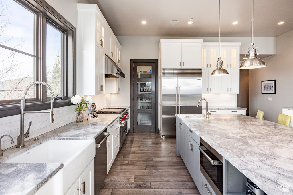 Kitchen with a sink, under cabinet range hood, premium appliances, recessed lighting, and tasteful backsplash