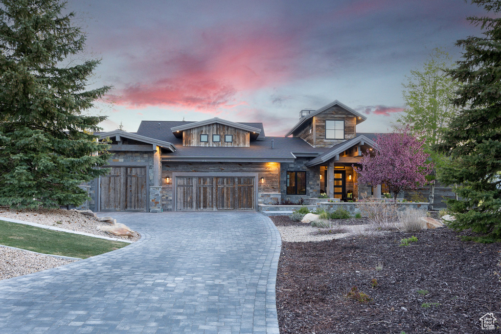 Modern home with stone siding, decorative driveway, an attached garage, and a porch