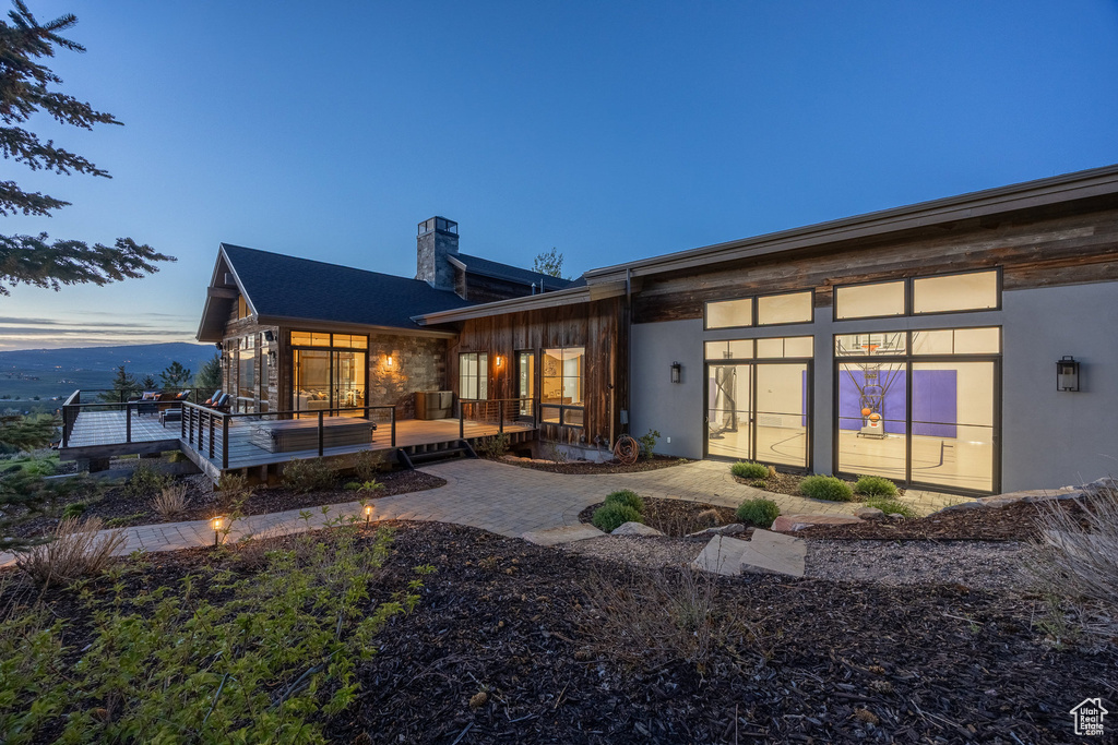 Back of house at dusk featuring a chimney and a deck