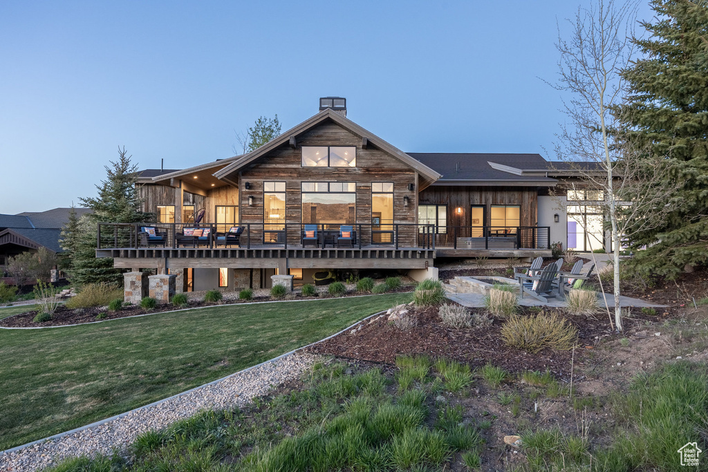 Back of property featuring a deck, a yard, a chimney, and stone siding