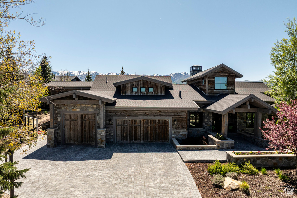 View of front of property with stone siding, a chimney, a garage, and decorative driveway