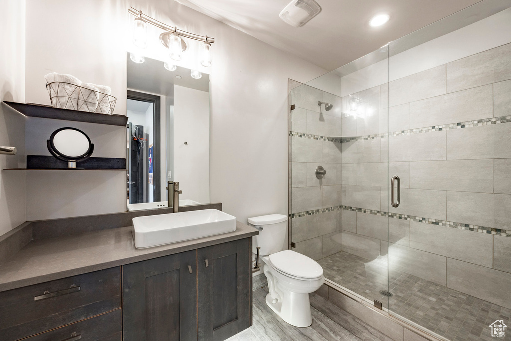 Bathroom featuring a shower stall, toilet, vanity, and wood finished floors