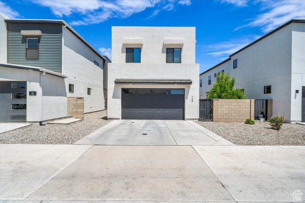 Contemporary house featuring an attached garage, driveway, stucco siding, and a gate