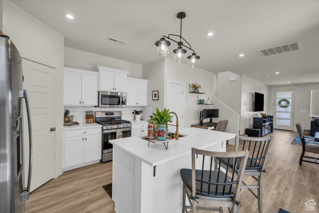 Kitchen featuring appliances with stainless steel finishes, light wood-style flooring, open floor plan, backsplash, and light countertops