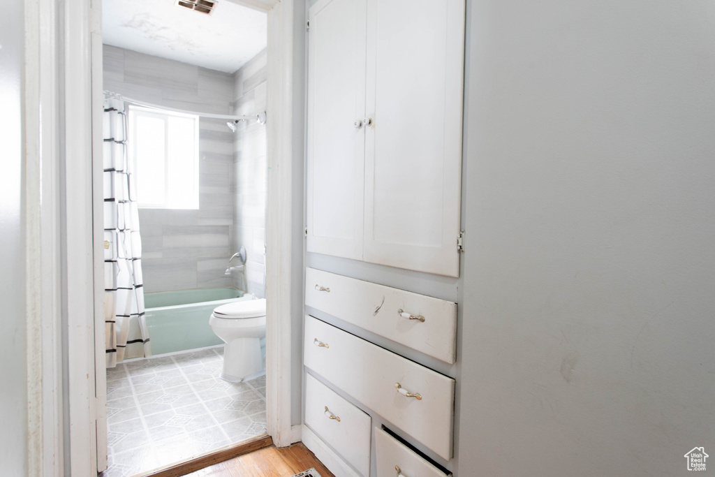 Full bath with toilet, shower / tub combo, and wood finished floors