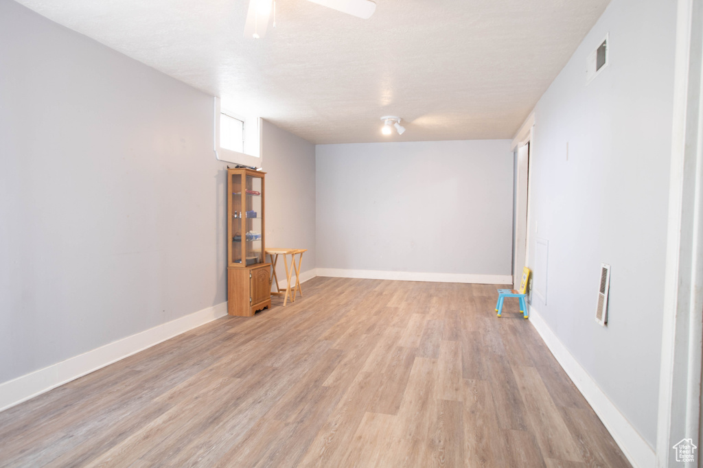 Basement with light wood-style floors, baseboards, and ceiling fan