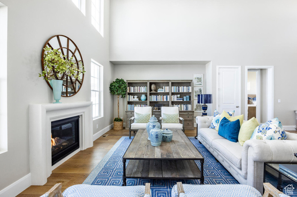 Living area with a high ceiling, baseboards, a glass covered fireplace, and wood finished floors