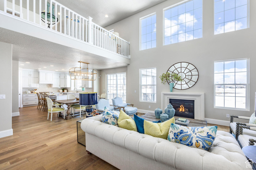 Living area with baseboards, a towering ceiling, light wood-type flooring, recessed lighting, and a glass covered fireplace