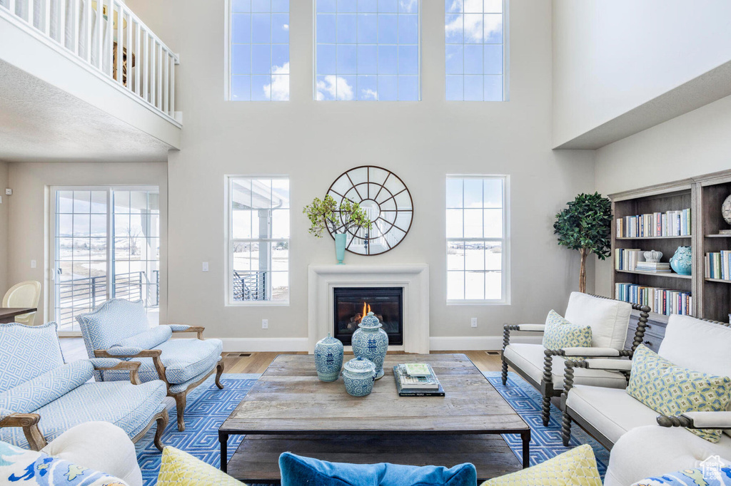 Living room with a towering ceiling, baseboards, wood finished floors, and a glass covered fireplace