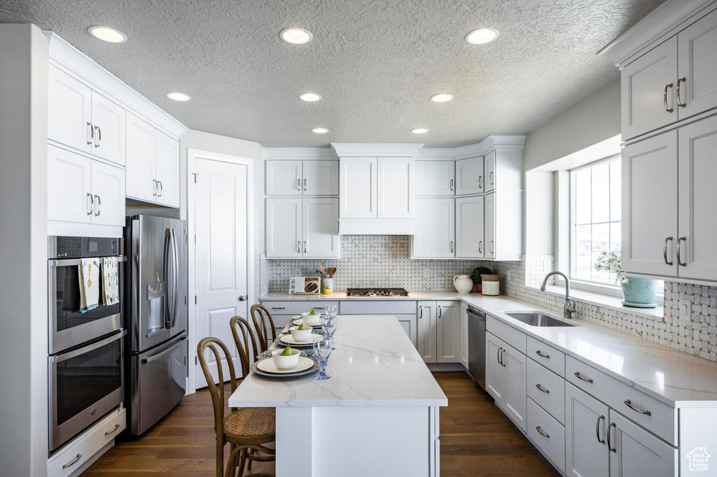 Kitchen featuring stainless steel appliances, a sink, a center island, dark wood-type flooring, and a textured ceiling