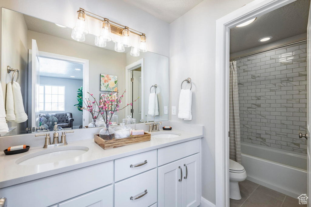 Full bath with double vanity, tile patterned flooring, toilet, and shower / bath combo with shower curtain