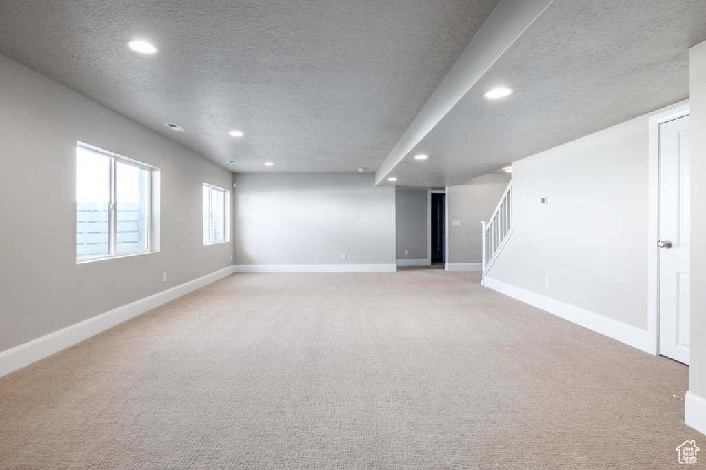 Basement featuring a textured ceiling, recessed lighting, stairs, light colored carpet, and baseboards