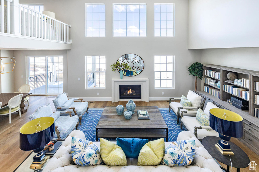 Living area featuring wood finished floors, a high ceiling, a warm lit fireplace, and baseboards
