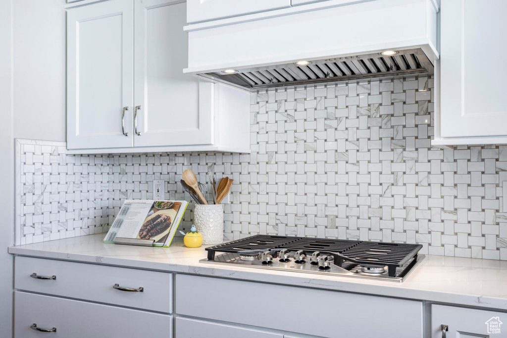 Kitchen with stainless steel gas stovetop, premium range hood, decorative backsplash, and white cabinetry