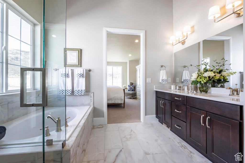 Ensuite bathroom featuring double vanity, a garden tub, baseboards, and marble look tiles
