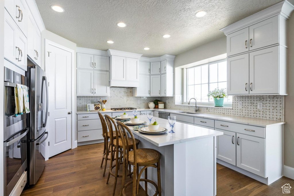 Kitchen with stainless steel appliances, a sink, dark wood-style flooring, a kitchen bar, and light countertops
