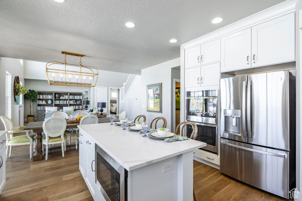 Kitchen with appliances with stainless steel finishes, a textured ceiling, a center island, white cabinets, and dark wood-style floors
