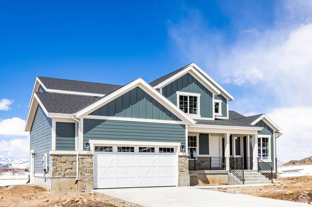 Craftsman-style home with covered porch, stone siding, driveway, and roof with shingles
