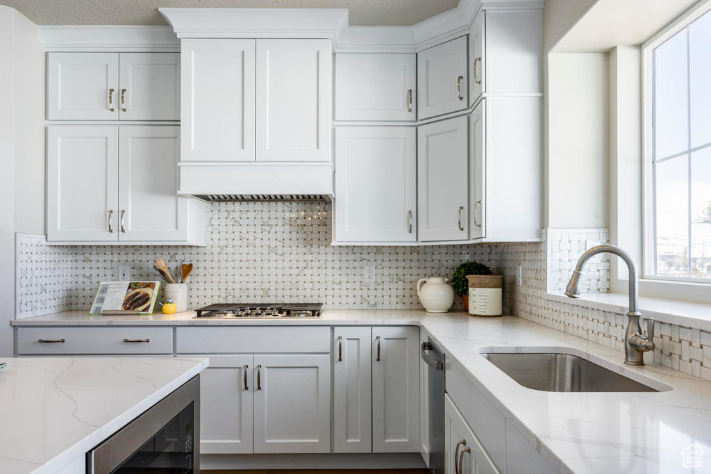 Kitchen featuring a sink, stainless steel appliances, backsplash, light stone counters, and beverage cooler